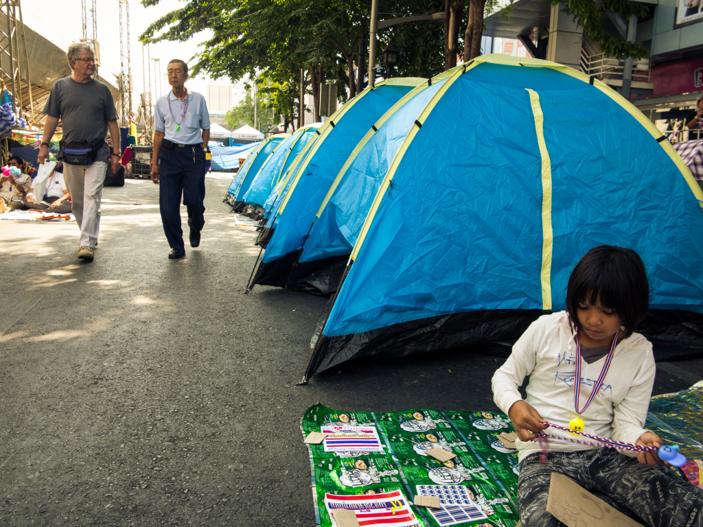 Bangkok Shutdown Child with tents. Making whistles to sell. 